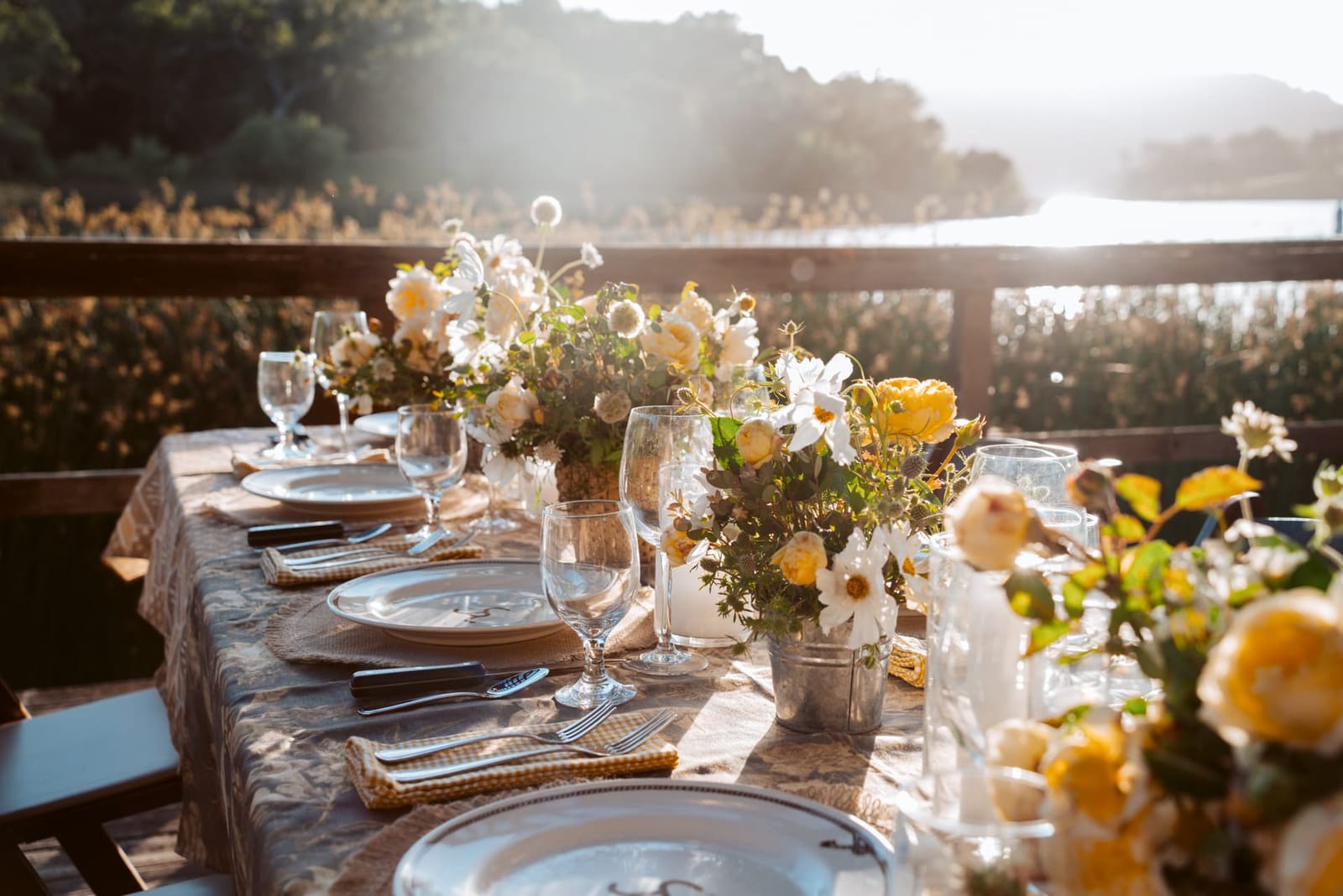 A long dinner table with flowers set beside a lake