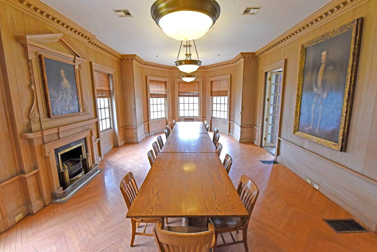 A pine-paneled room with a long table and chairs near a fireplace