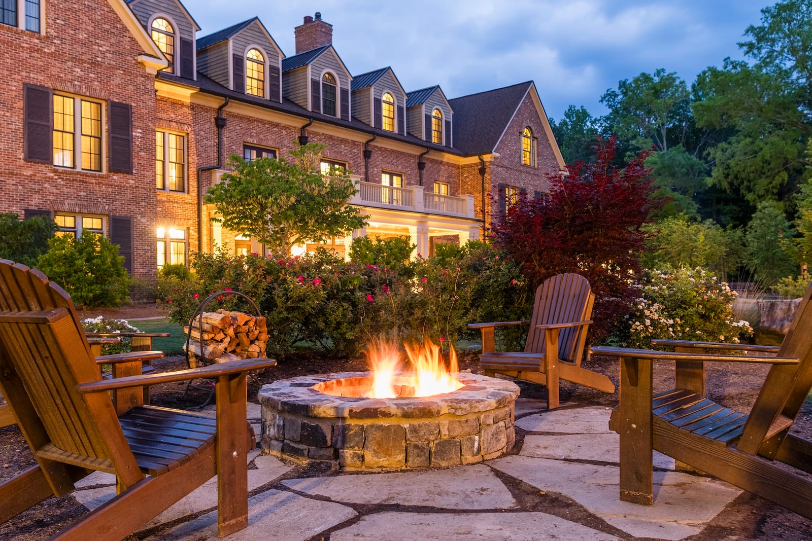 Adirondack chairs around a fire pit outside a brick inn at dusk
