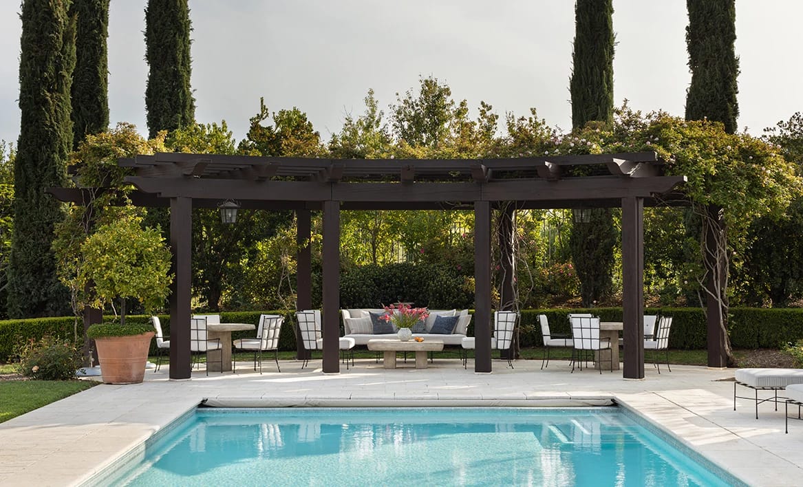 A pool beside a shaded pergola lounge in a walled garden