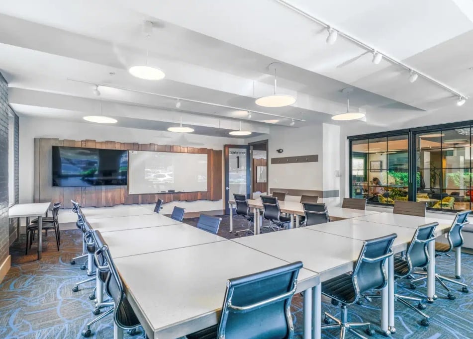 A conference room with tables set in a U shape, a screen and a whiteboard