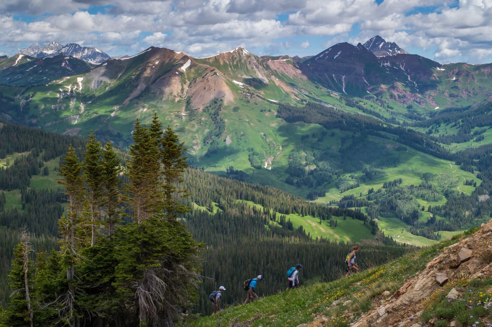 Hikers on a ridge above green valleys and the Elk Mountains