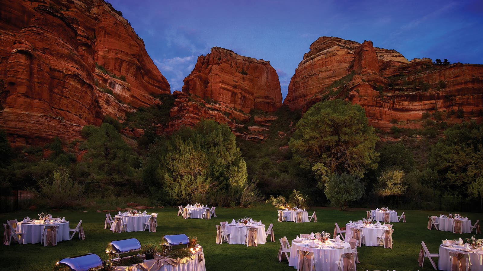 Dinner tables on the Enchantment Circle lawn at dusk beneath red rock canyon walls