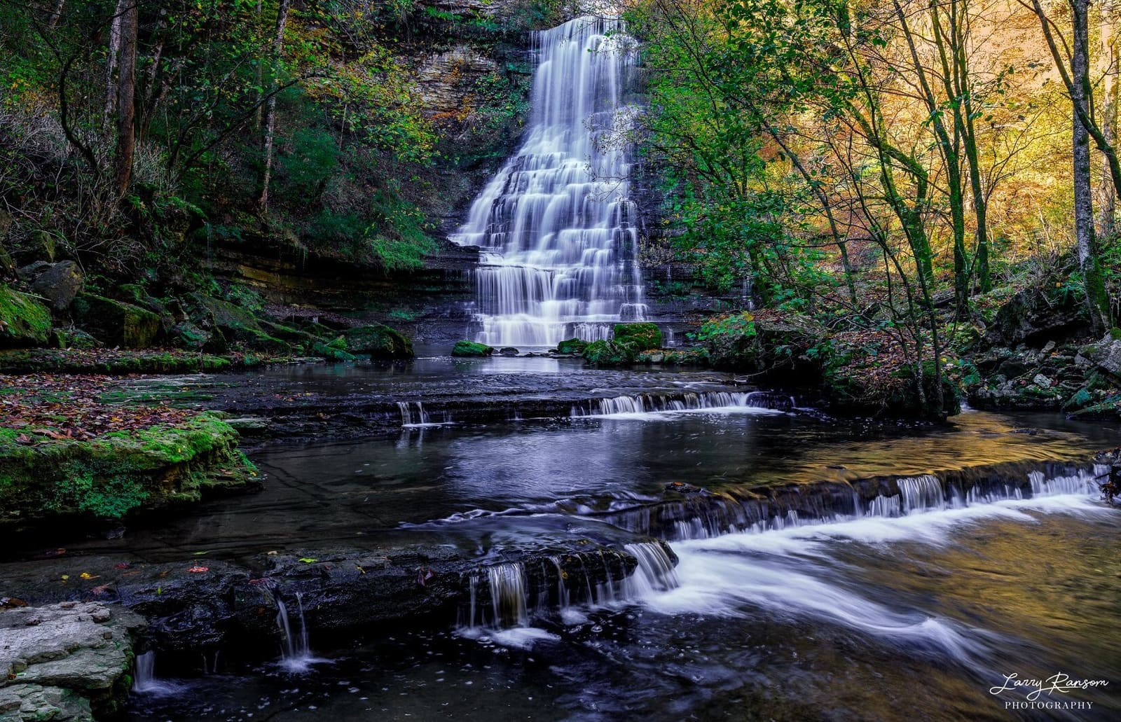 Waterfall spilling over rock ledges into a creek in autumn woods
