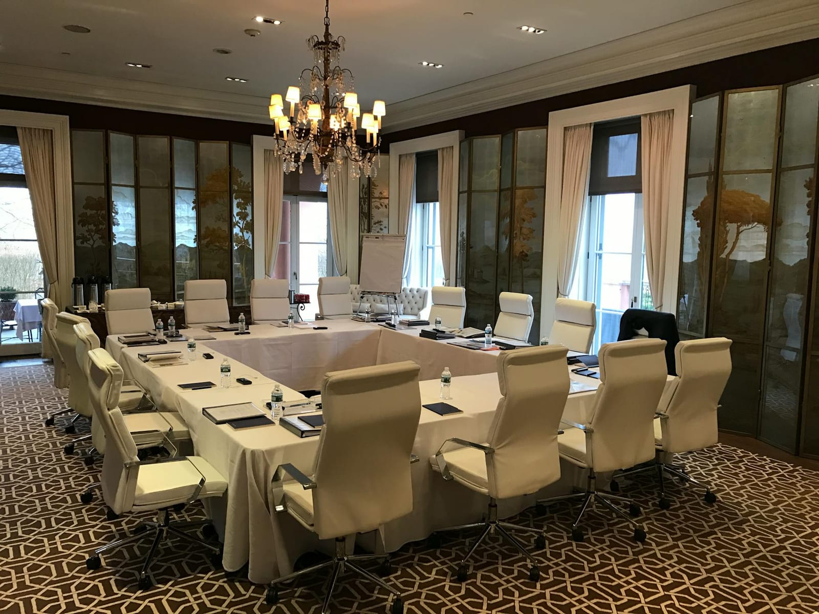 A boardroom table with white leather chairs under a crystal chandelier