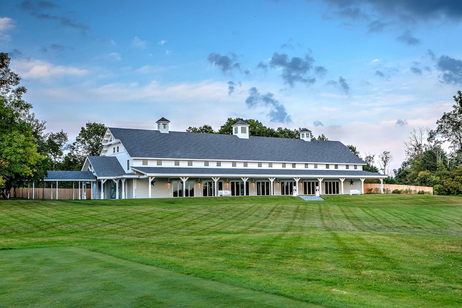 A large white event barn on a wide green lawn under a blue sky