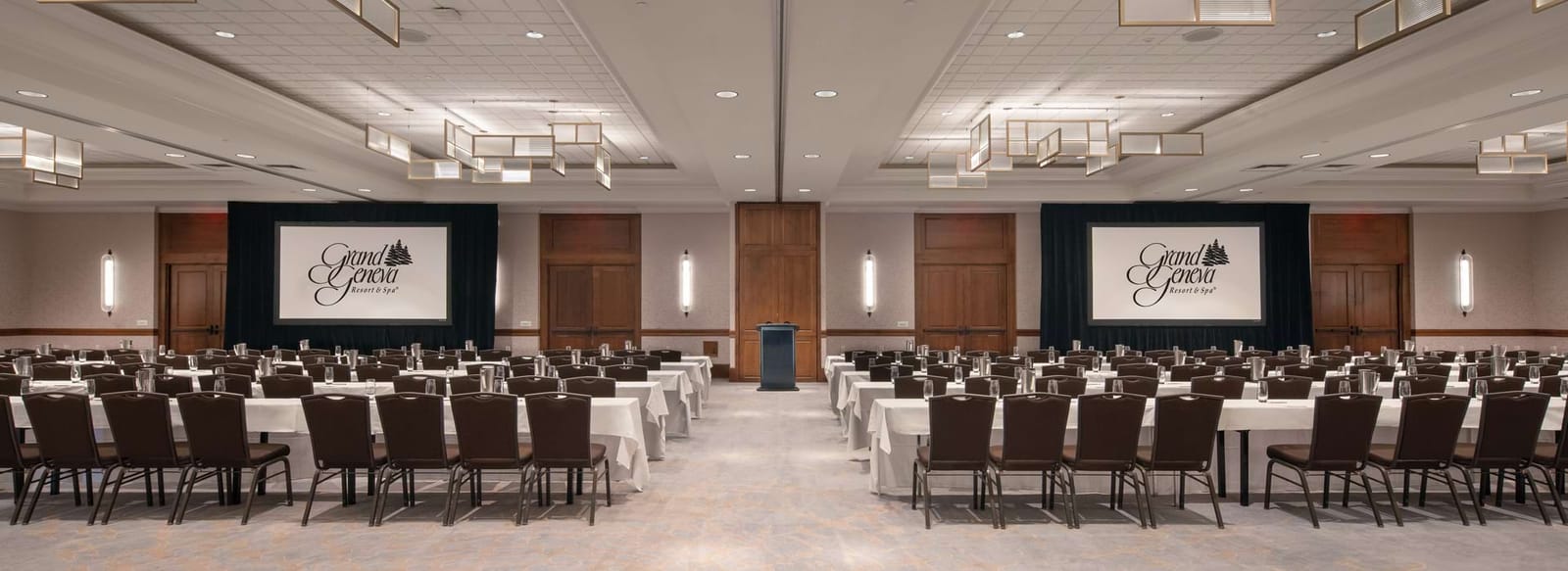 A ballroom set classroom style with rows of tables and two screens