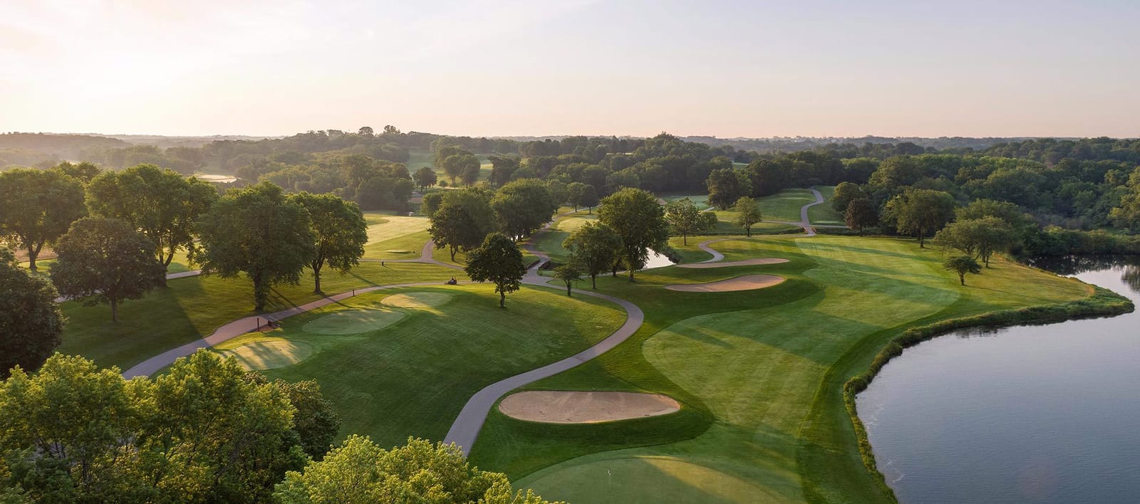 An aerial view of a golf hole with sand bunkers beside a pond
