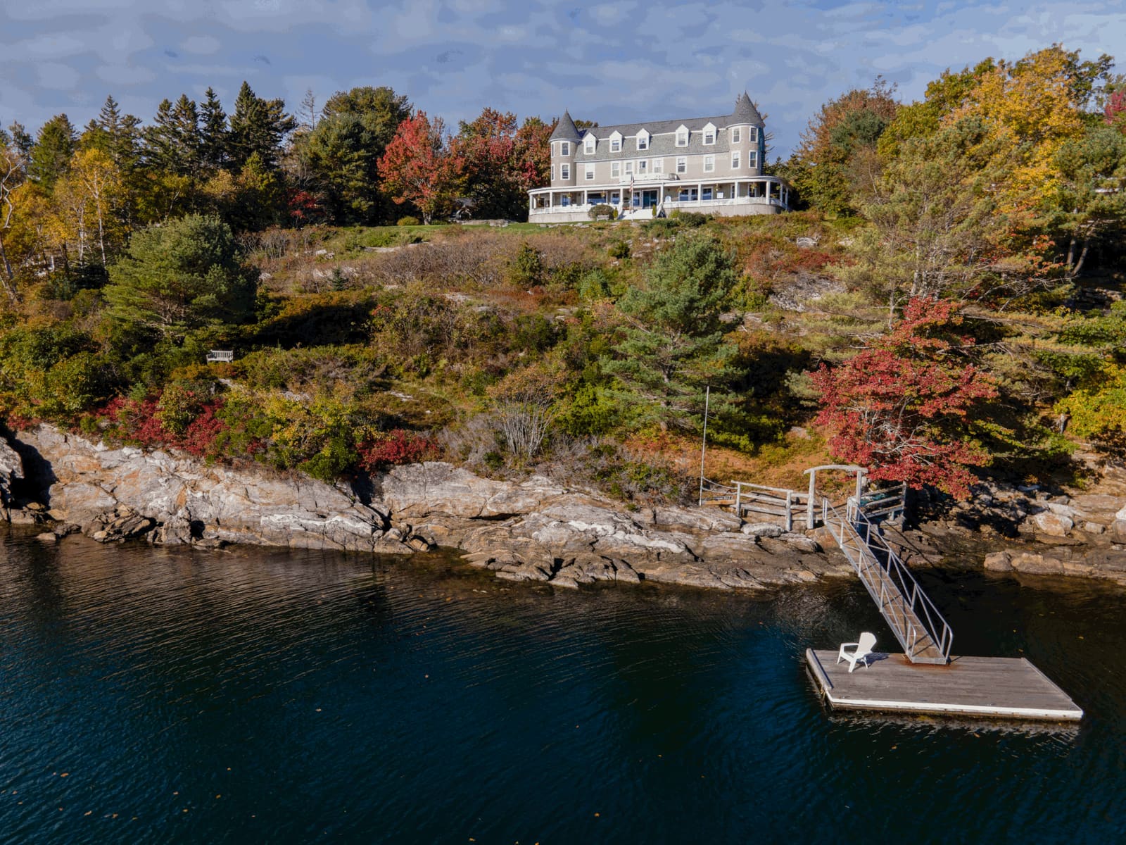 Aerial view of the turreted inn on its rocky bluff above the harbor and dock in fall