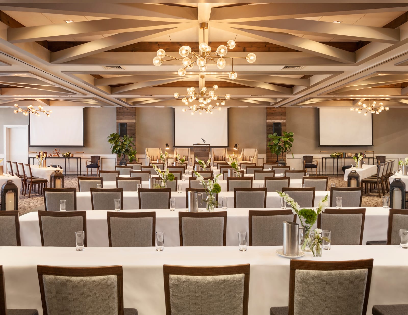 A bright hall with chandeliers set with rows of tables for a meeting
