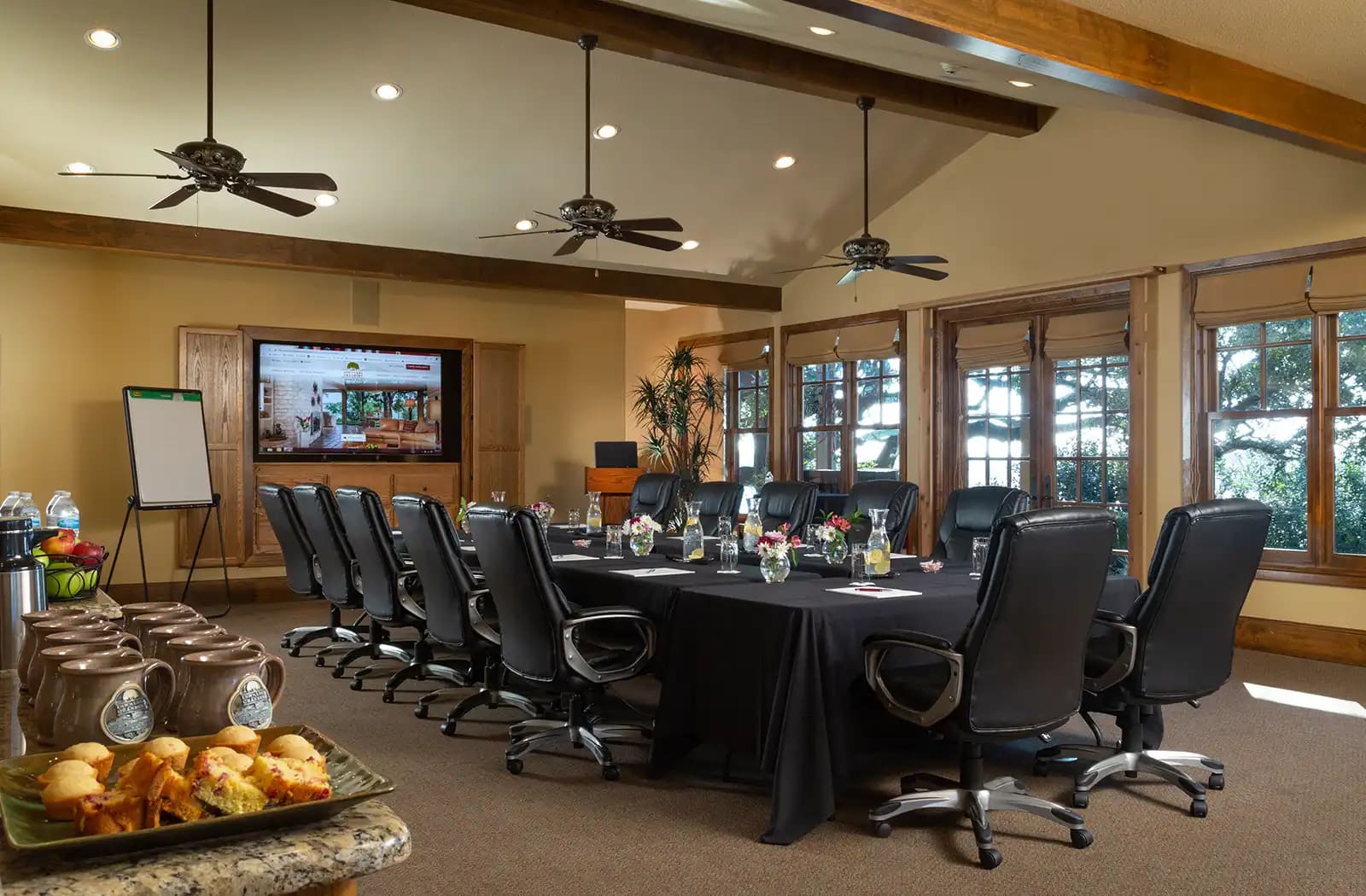 Conference room set boardroom style with executive chairs, a large screen and windows to the trees