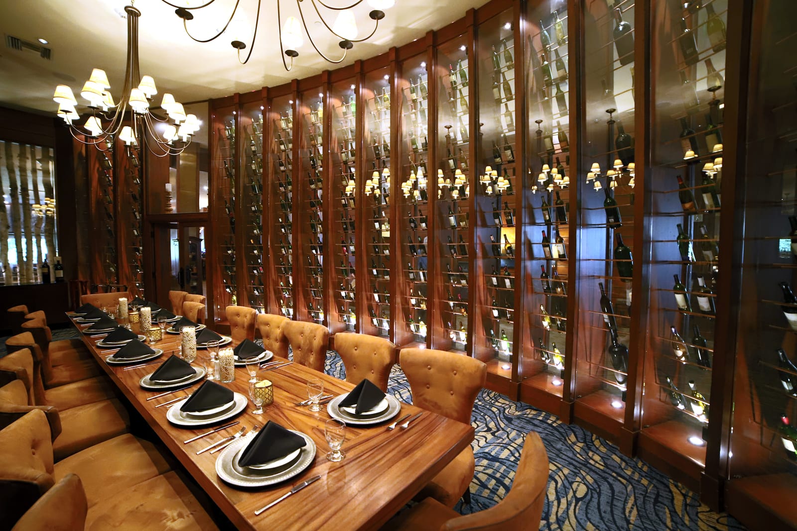 A wood-paneled boardroom with a long table under chandeliers