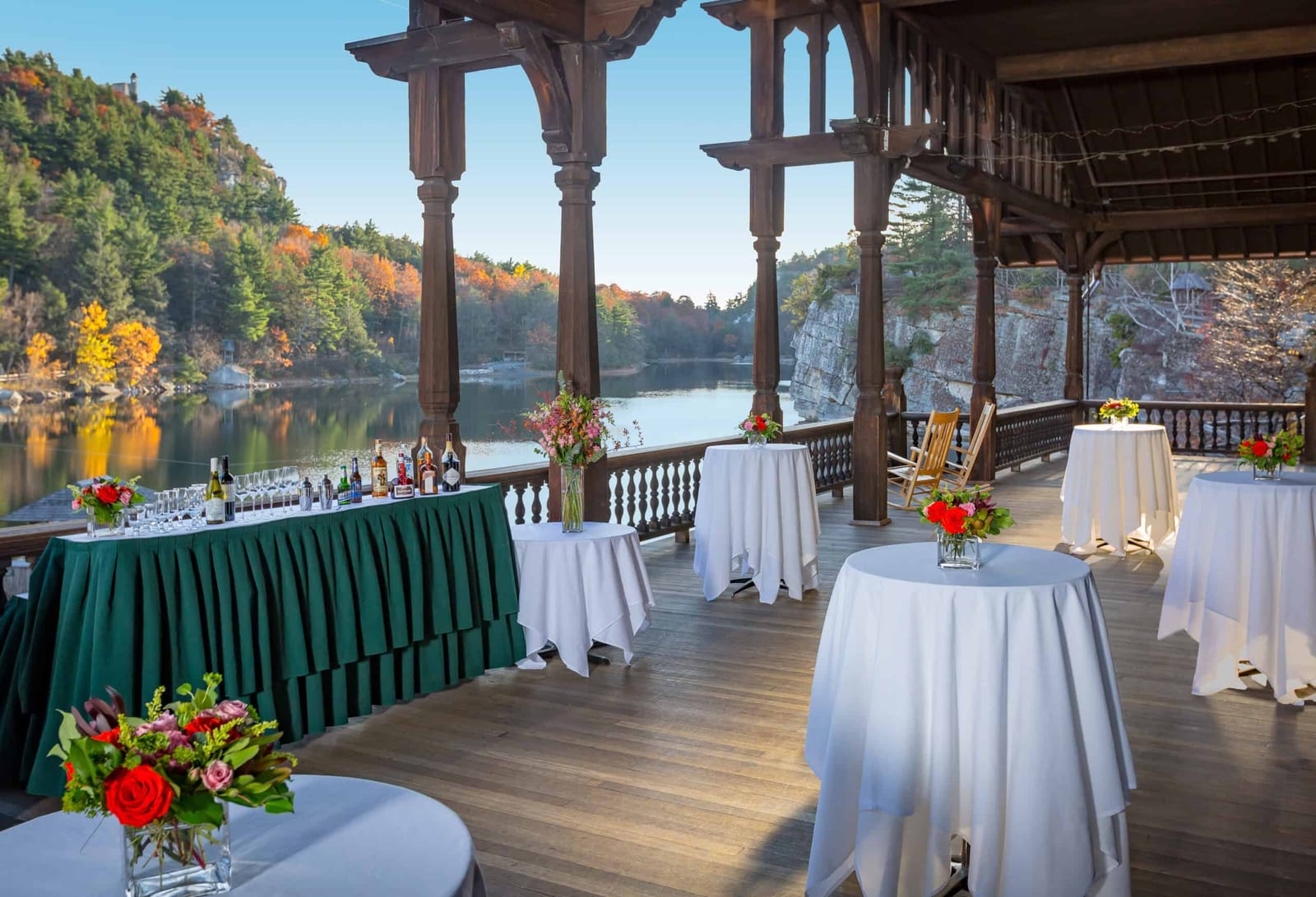 A covered wooden porch set with cocktail tables above the lake in autumn
