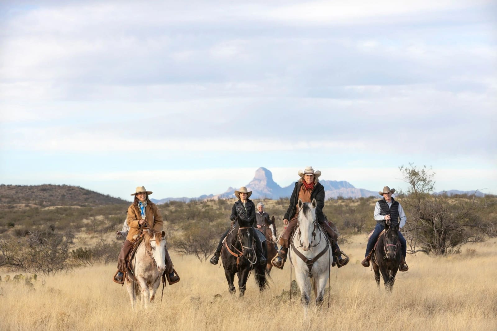 Group on horseback in desert grassland with Baboquivari Peak behind