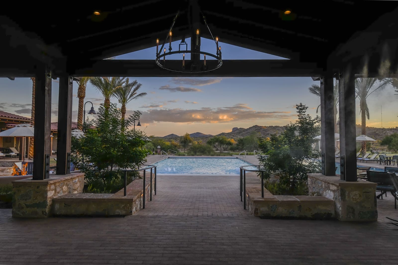 View from a covered stone pavilion across the pool to desert mountains at sunset