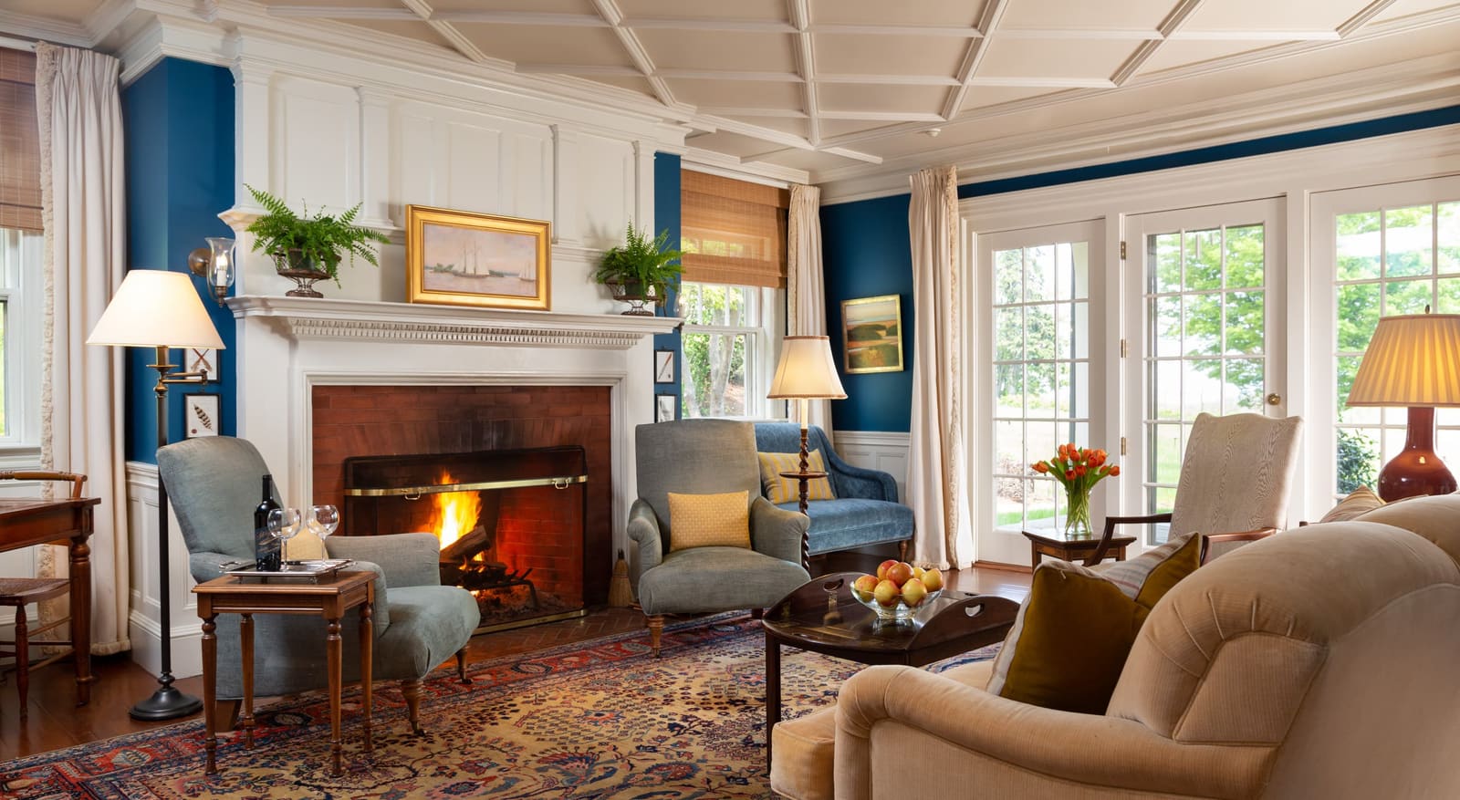 Inn living room with a lit fireplace, armchairs and French doors to the lawn