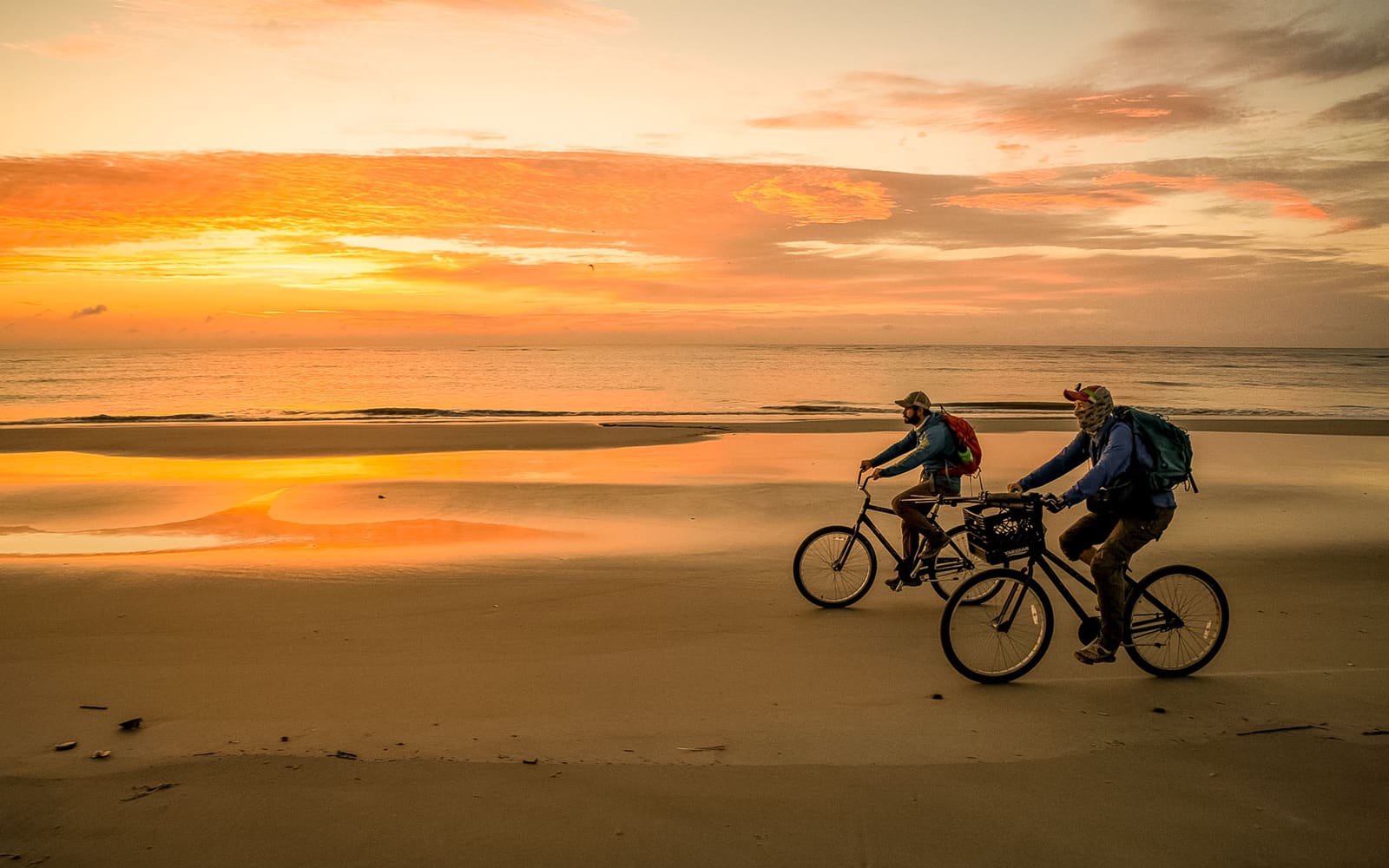 Two people biking on the island beach at sunset
