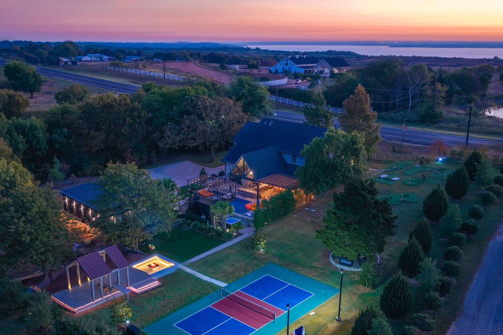 Aerial view of the estate at dusk with pool, pavilion, pickleball court and Lavon Lake on the horizon