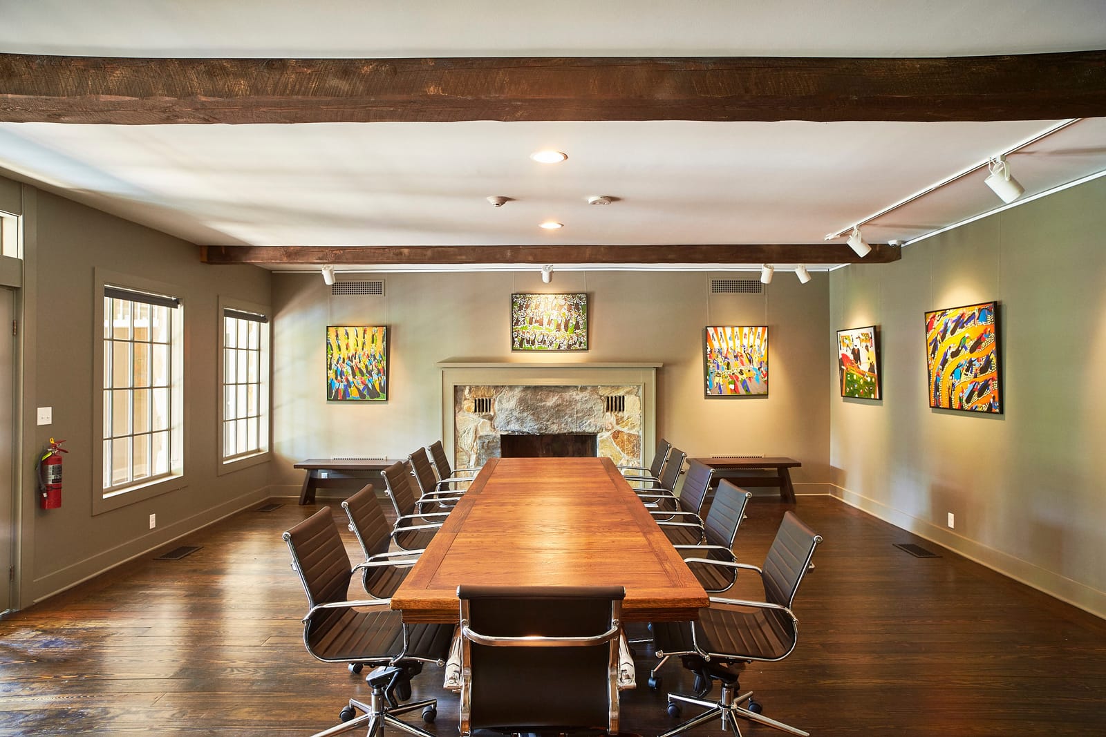 A long wooden boardroom table in a gallery hung with colorful paintings